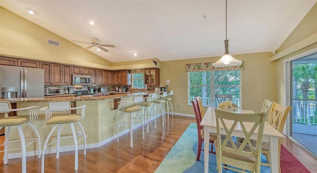 kitchen featuring appliances with stainless steel finishes, a breakfast bar area, vaulted ceiling, light hardwood / wood-style floors, and pendant lighting