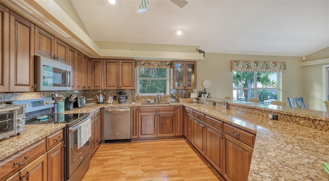 kitchen with appliances with stainless steel finishes, a healthy amount of sunlight, tasteful backsplash, and light hardwood / wood-style flooring