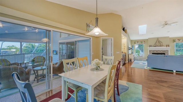 dining space with hardwood / wood-style flooring, a stone fireplace, high vaulted ceiling, and ceiling fan