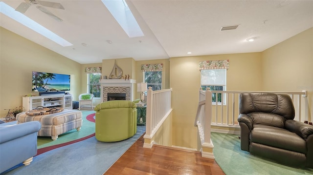 living room featuring wood-type flooring, ceiling fan, a stone fireplace, and lofted ceiling with skylight