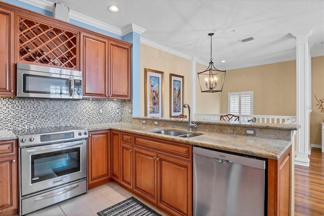 kitchen featuring sink, appliances with stainless steel finishes, hanging light fixtures, light stone counters, and kitchen peninsula