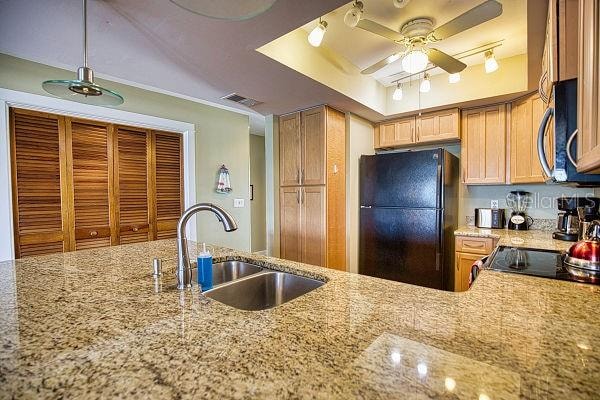 kitchen with black fridge, ceiling fan, track lighting, light stone counters, and sink