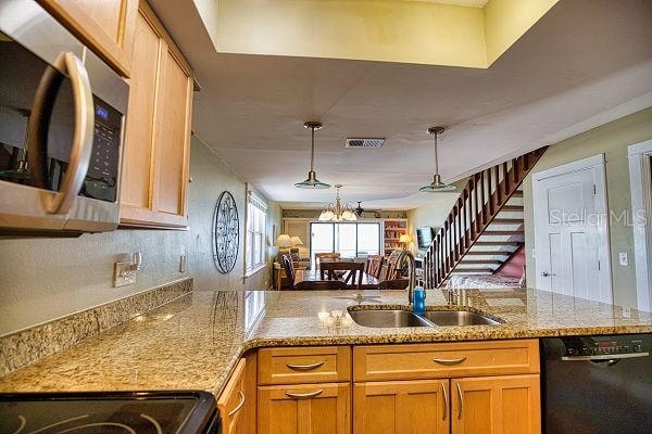 kitchen with light stone counters, sink, a notable chandelier, black dishwasher, and pendant lighting