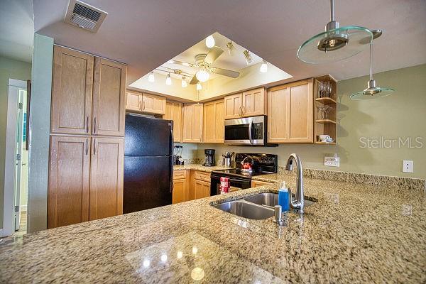 kitchen with light brown cabinets, ceiling fan, black appliances, light stone counters, and sink