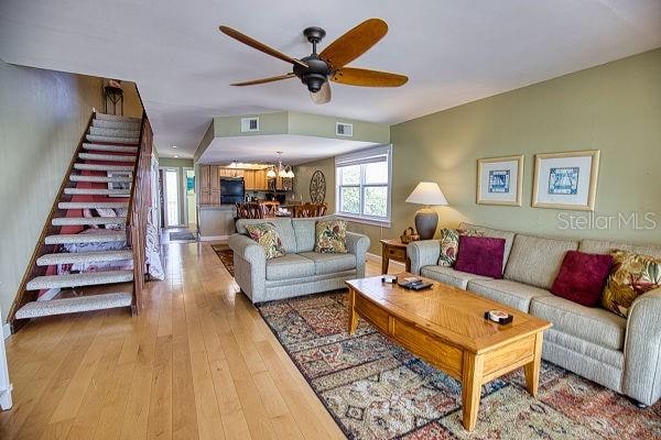 living room featuring ceiling fan with notable chandelier and light hardwood / wood-style flooring