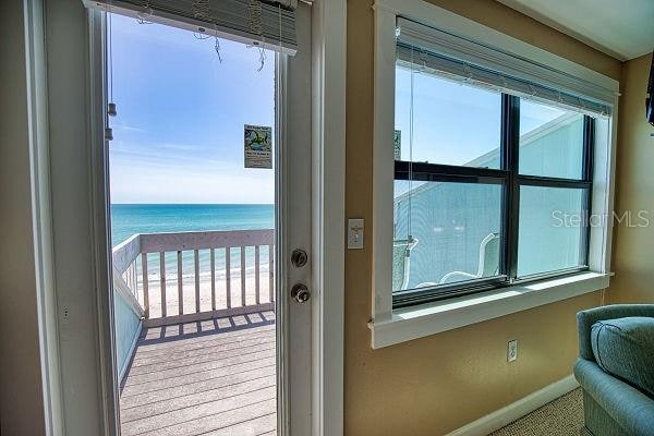 doorway featuring a wealth of natural light, light carpet, a beach view, and a water view