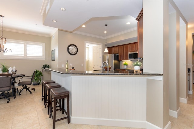 kitchen with a kitchen bar, hanging light fixtures, dark stone countertops, and stainless steel appliances