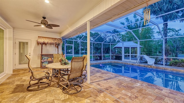 view of pool with a water slide, glass enclosure, ceiling fan, and a patio