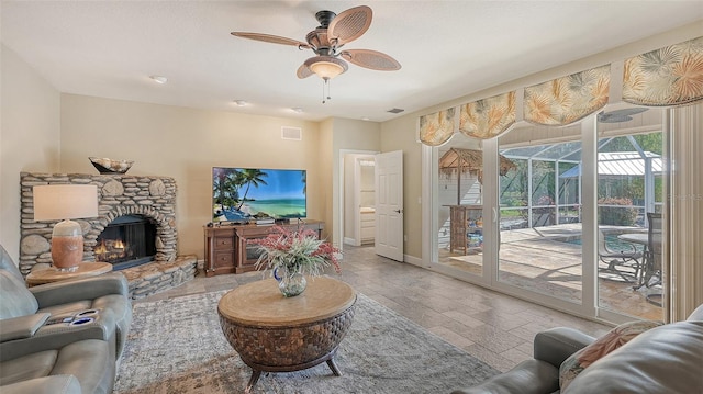 living room with ceiling fan and a stone fireplace