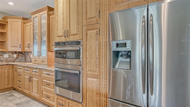 kitchen with light stone countertops, backsplash, stainless steel appliances, light tile flooring, and light brown cabinetry