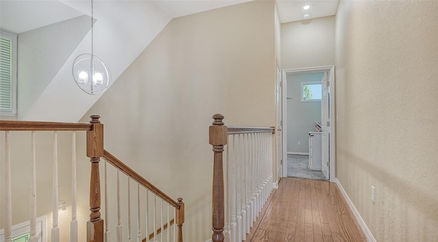 hallway with light hardwood / wood-style flooring, a notable chandelier, and lofted ceiling