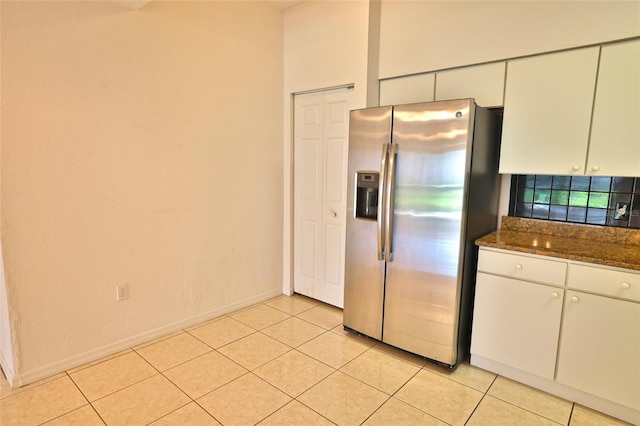 kitchen with white cabinets, light tile patterned floors, stainless steel fridge with ice dispenser, and dark stone counters