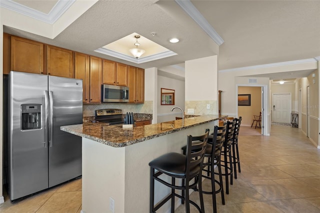 kitchen with a breakfast bar, dark stone countertops, ornamental molding, kitchen peninsula, and stainless steel appliances