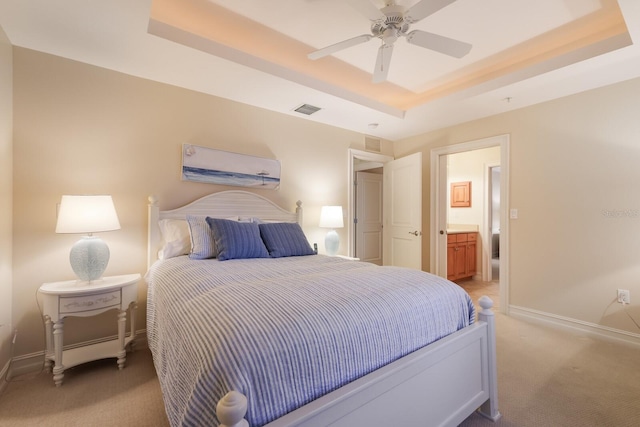 carpeted bedroom featuring ceiling fan, a raised ceiling, and ensuite bathroom