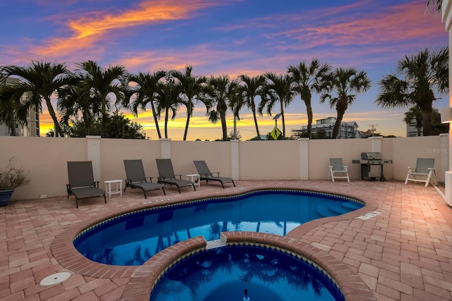 pool at dusk with grilling area, an in ground hot tub, and a patio