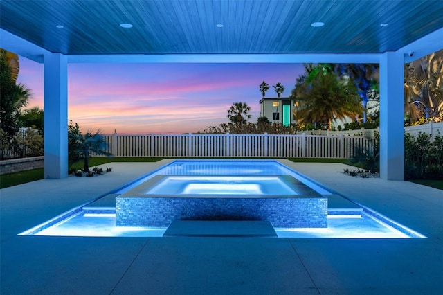 pool at dusk with a patio and an in ground hot tub