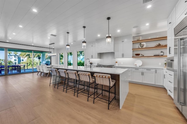 kitchen with white cabinets, a breakfast bar, appliances with stainless steel finishes, light hardwood / wood-style flooring, and a kitchen island with sink