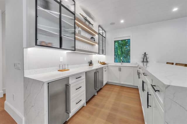 kitchen with decorative backsplash, white cabinetry, light stone counters, and light wood-type flooring