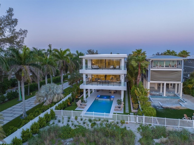 back house at dusk with a balcony, a pool with hot tub, and a patio area