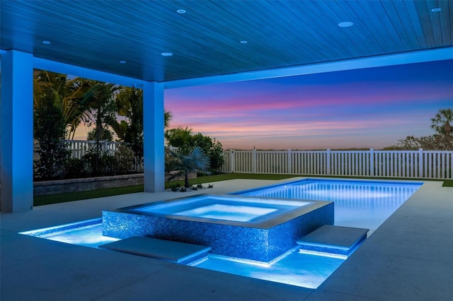 pool at dusk featuring an in ground hot tub and a patio