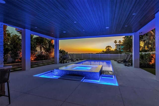 pool at dusk featuring an in ground hot tub and a patio