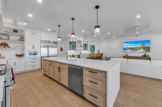 kitchen featuring light brown cabinetry, stainless steel appliances, a large island, light stone countertops, and light hardwood / wood-style floors