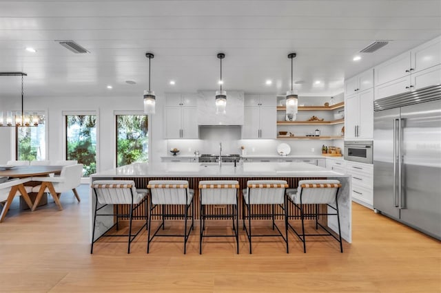 kitchen with white cabinets, light hardwood / wood-style flooring, stainless steel appliances, and an island with sink