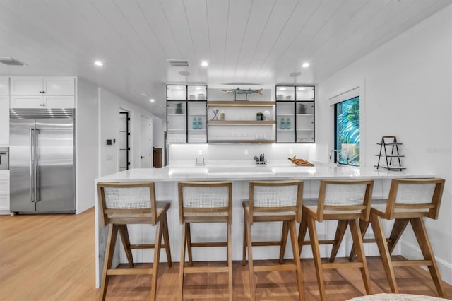 kitchen featuring white cabinetry, wooden ceiling, a kitchen breakfast bar, stainless steel built in fridge, and light hardwood / wood-style floors