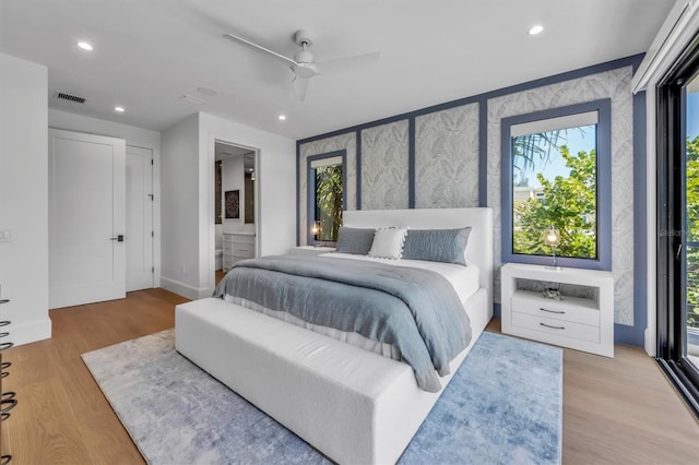 bedroom with multiple windows, ensuite bath, ceiling fan, and light wood-type flooring