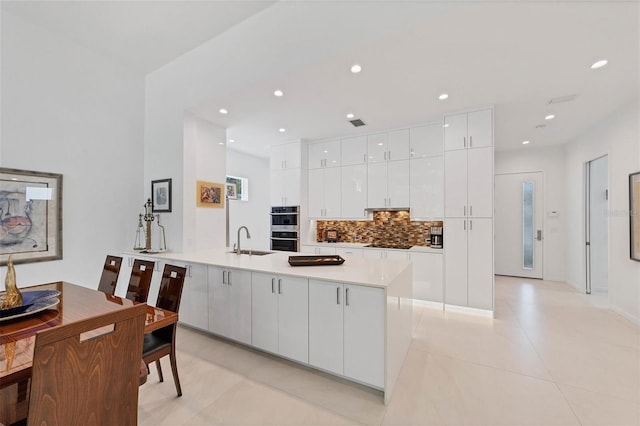 kitchen featuring white cabinets, double oven, kitchen peninsula, light tile floors, and sink