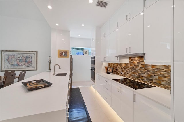 kitchen with black electric stovetop, light tile flooring, white cabinetry, backsplash, and sink