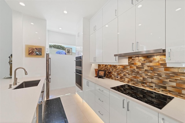 kitchen featuring light tile floors, sink, backsplash, white cabinetry, and black electric stovetop