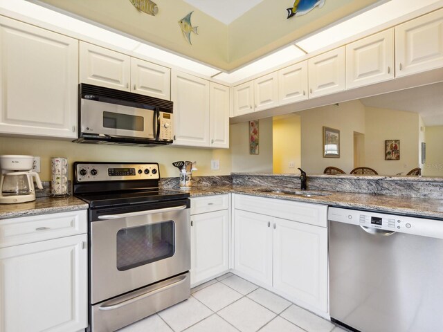 kitchen featuring stainless steel appliances, dark stone counters, white cabinets, sink, and light tile floors