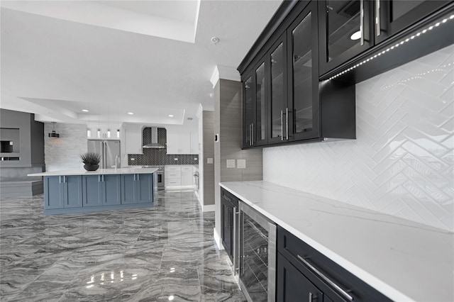 kitchen featuring wall chimney exhaust hood, hanging light fixtures, beverage cooler, stainless steel refrigerator, and tasteful backsplash