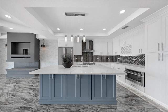 kitchen with white cabinets, wall chimney exhaust hood, stainless steel appliances, and a tray ceiling