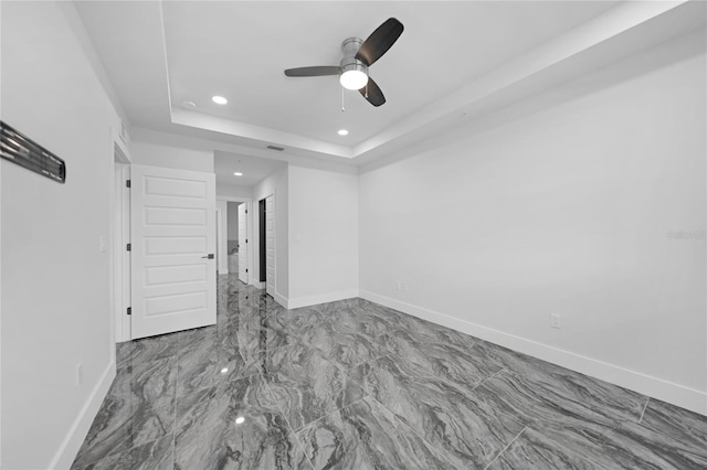 empty room with a raised ceiling, ceiling fan, and tile flooring