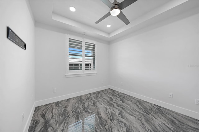 tiled empty room featuring ceiling fan and a tray ceiling