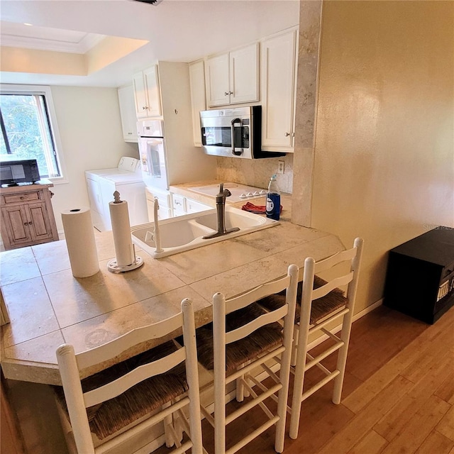 dining area with sink, washer and dryer, wood-type flooring, a raised ceiling, and ornamental molding