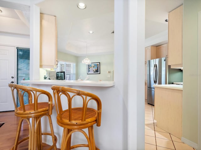 kitchen featuring stainless steel refrigerator, a kitchen breakfast bar, decorative light fixtures, and light brown cabinets