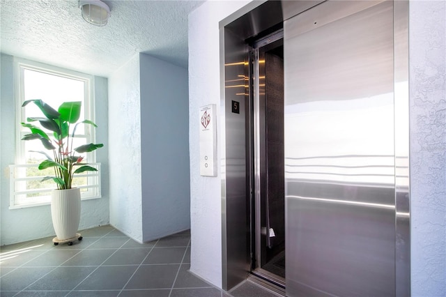 hall featuring a textured ceiling, elevator, and dark tile patterned flooring