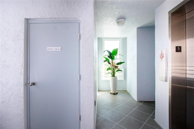 corridor featuring elevator, a textured ceiling, dark tile patterned floors, and a healthy amount of sunlight