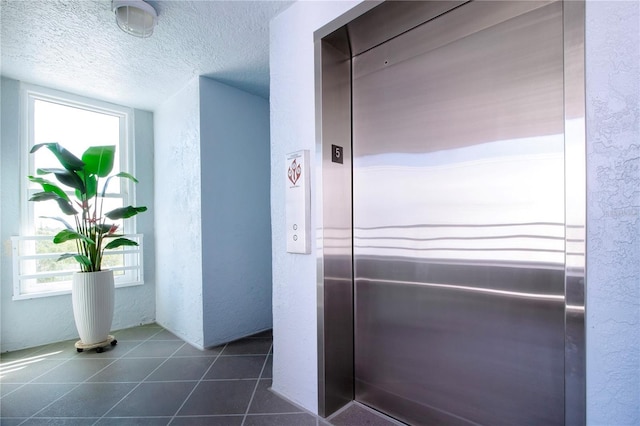 corridor with elevator, a textured ceiling, dark tile patterned floors, and plenty of natural light