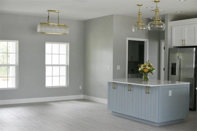 kitchen featuring light wood-type flooring, kitchen peninsula, pendant lighting, stainless steel fridge with ice dispenser, and a breakfast bar