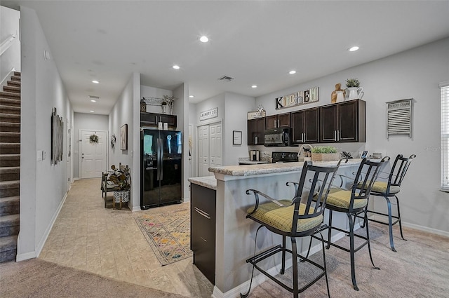 kitchen featuring kitchen peninsula, light carpet, black appliances, and a kitchen bar