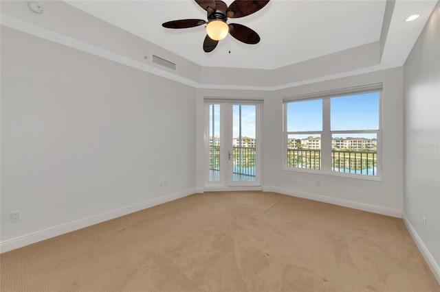 empty room with a tray ceiling, ceiling fan, and light colored carpet