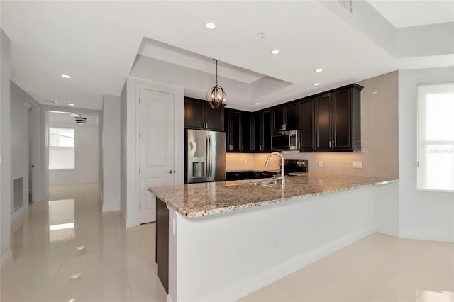 kitchen featuring appliances with stainless steel finishes, tasteful backsplash, decorative light fixtures, light stone counters, and kitchen peninsula