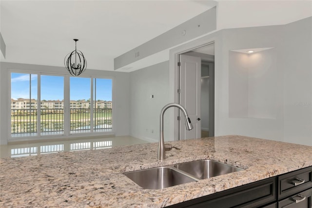 kitchen featuring decorative light fixtures, light stone counters, sink, and an inviting chandelier