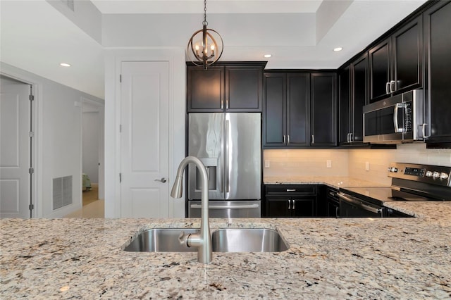 kitchen featuring decorative backsplash, appliances with stainless steel finishes, light stone counters, sink, and decorative light fixtures