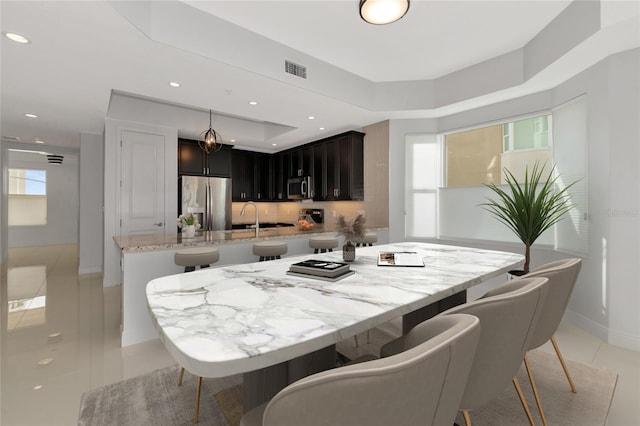 kitchen with appliances with stainless steel finishes, visible vents, light stone counters, and a kitchen bar