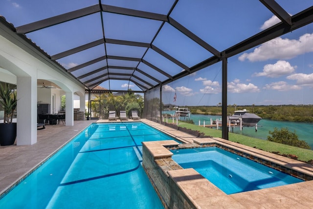 view of pool with glass enclosure, a patio area, a water view, and an in ground hot tub